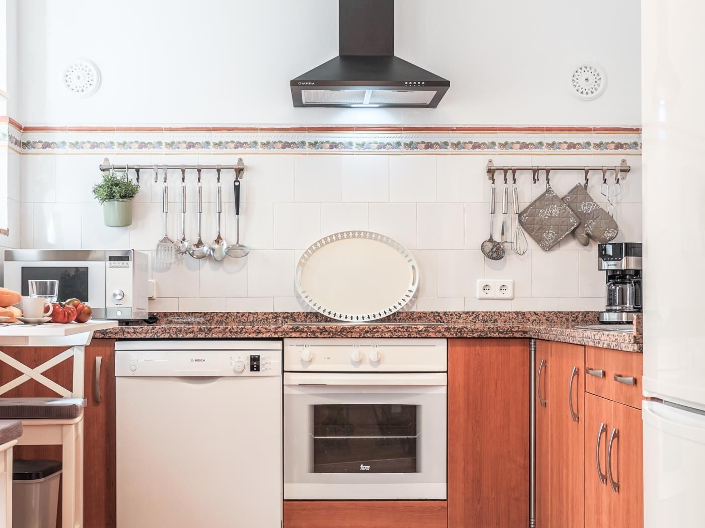 A modern kitchen with white appliances, a Bosch dishwasher, a Teka oven, and a black range hood.