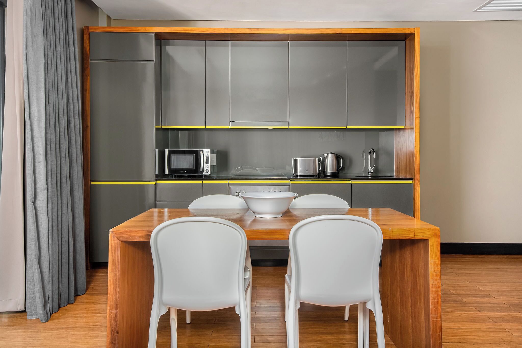 A compact kitchen with a wooden table and white chairs, a microwave, a kettle, and a sink.