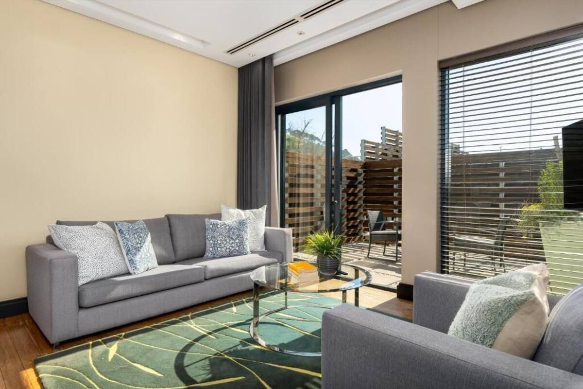 A modern living room with a grey sofa, a glass coffee table, and a green patterned rug.