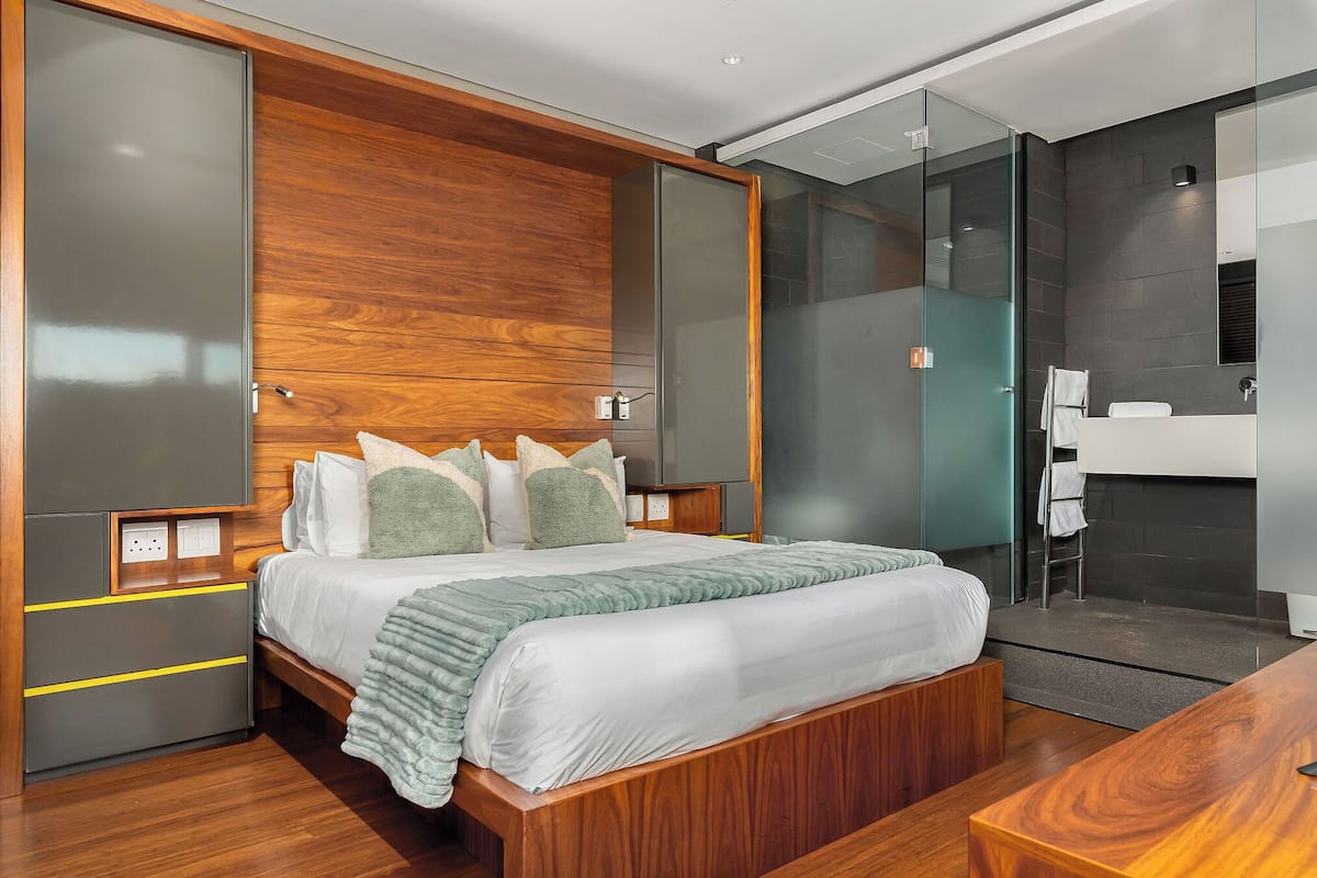 A modern bedroom with a wooden headboard, a large bed, a bedside table, and a built-in wardrobe.