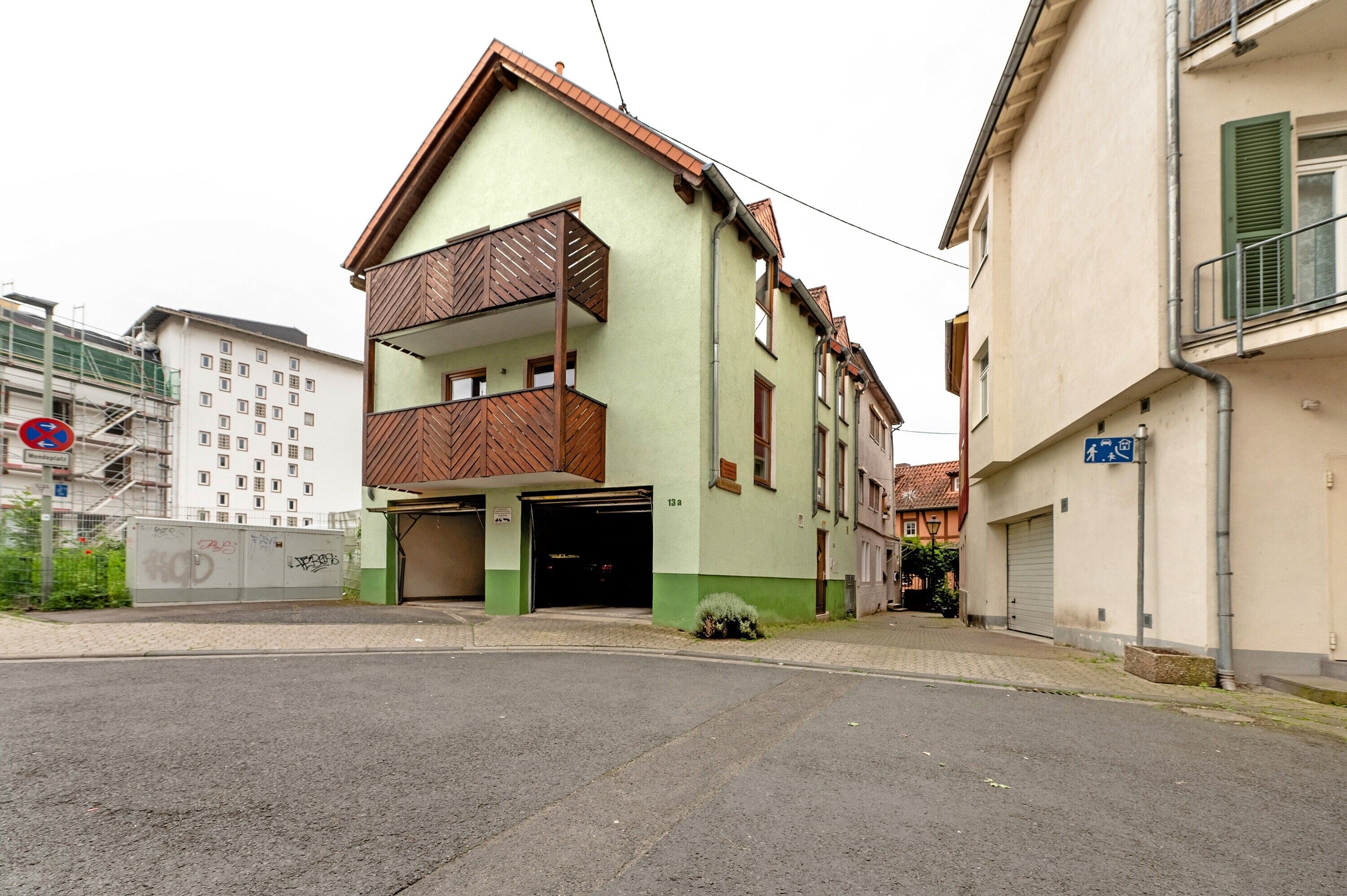 Un bâtiment à deux étages, doté d’une façade verte, d’un balcon au deuxième étage et d’une entrée de garage.