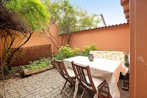 Eine Terrasse mit Tisch und Stühlen, umgeben von Pflanzen und einer Backsteinmauer.