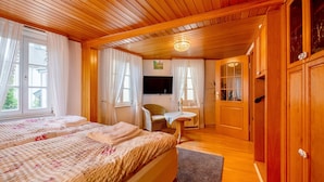 Una habitación con paneles de madera, una cama, una silla, una mesita y un televisor.
