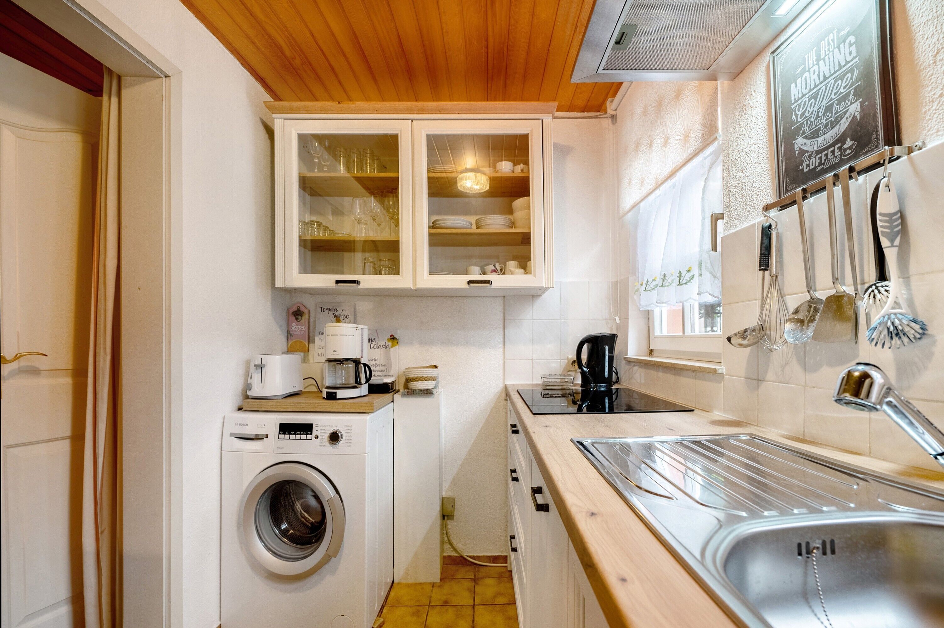 A compact kitchen with a washing machine, a coffee maker, and a sink.