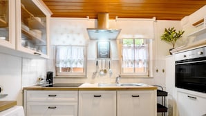 Una cocina con gabinetes blancos, una campana extractora de acero inoxidable, un lavamanos y una estufa.