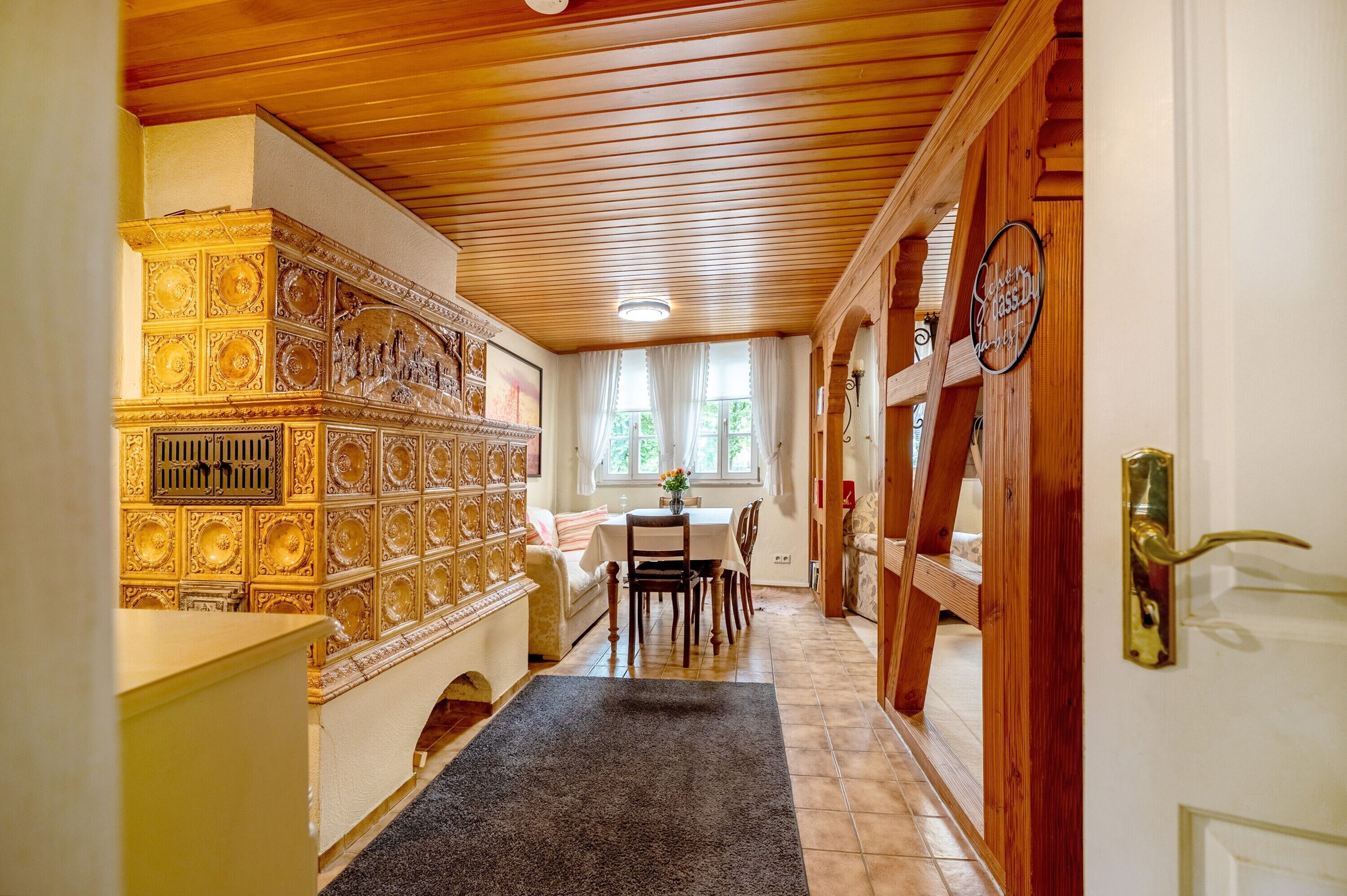 Ein Korridor mit Holzboden, ein Essbereich mit Tisch und Stühlen sowie eine Wand mit aufwendigen Verzierungen.