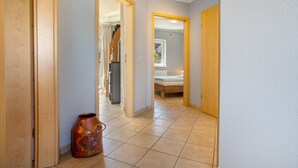 Un pasillo con una puerta de madera, suelo de baldosas y una pequeña maceta decorativa.