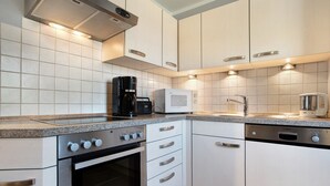 Cocina moderna con alacenas blancas, horno empotrado, microondas, cafetera y lavavajillas.