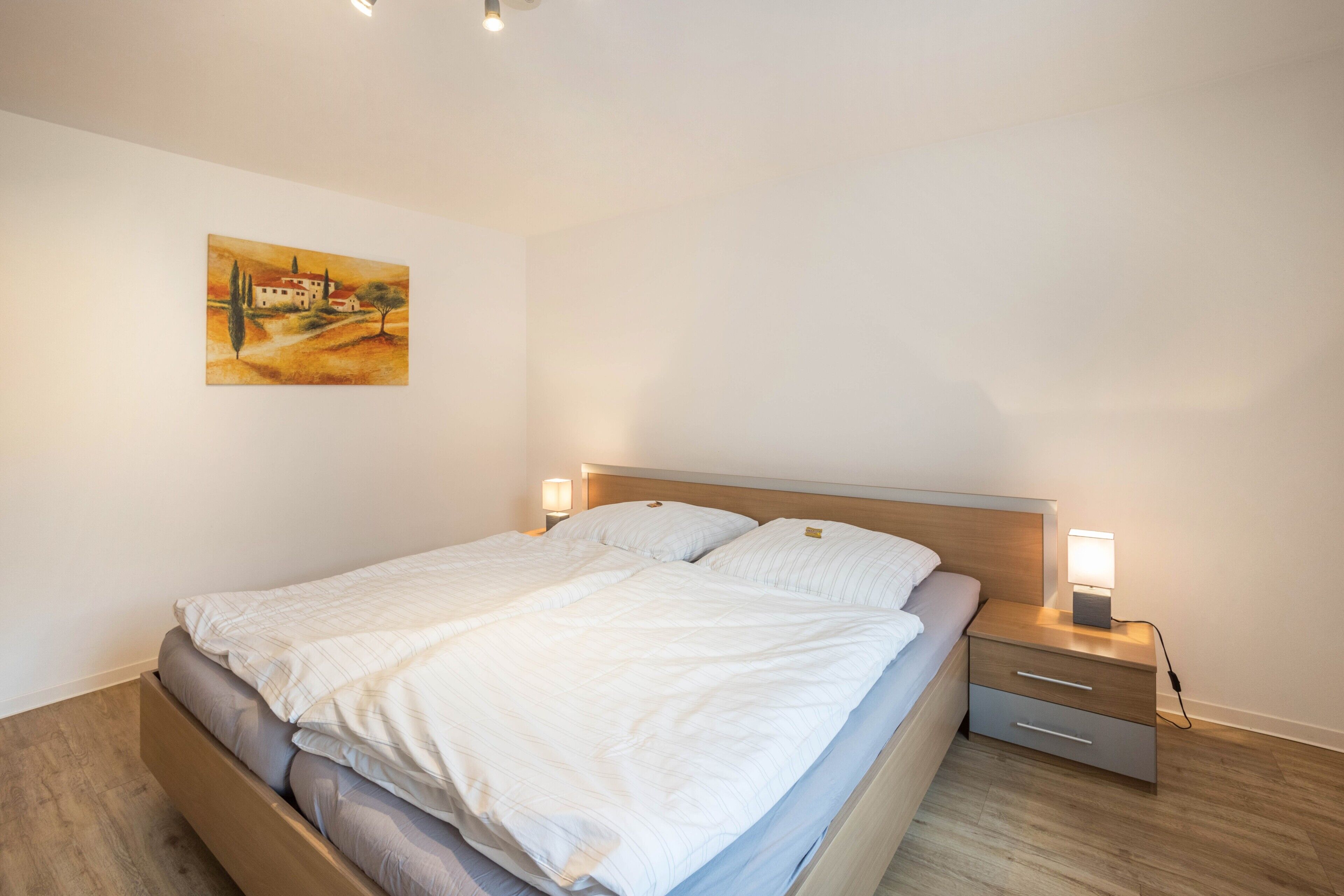 A bedroom with a bed, bedside tables, and a painting on the wall.