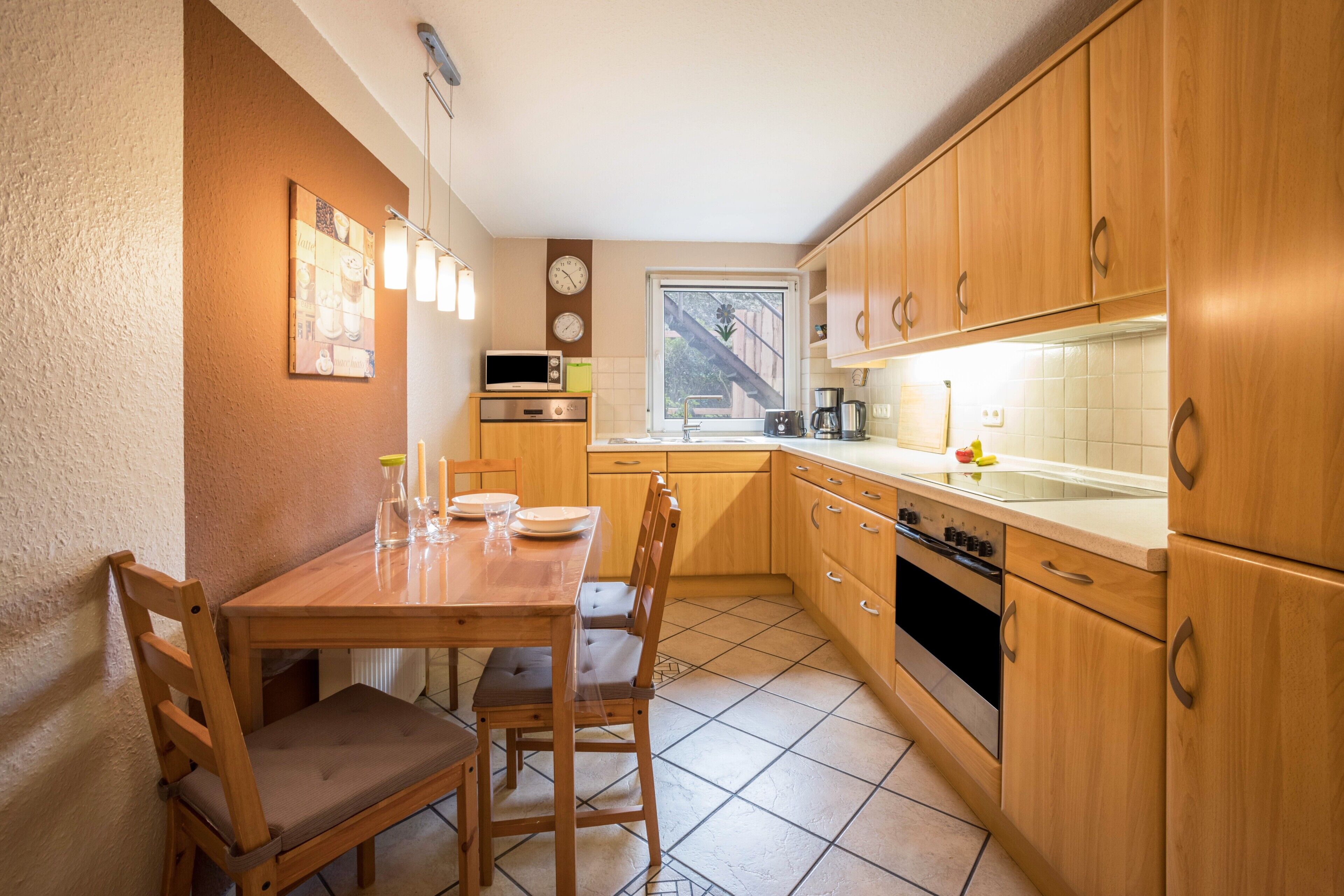 Une cuisine compacte avec des meubles en bois, une table à manger avec des chaises, un four à micro-ondes et une fenêtre donnant sur un escalier.