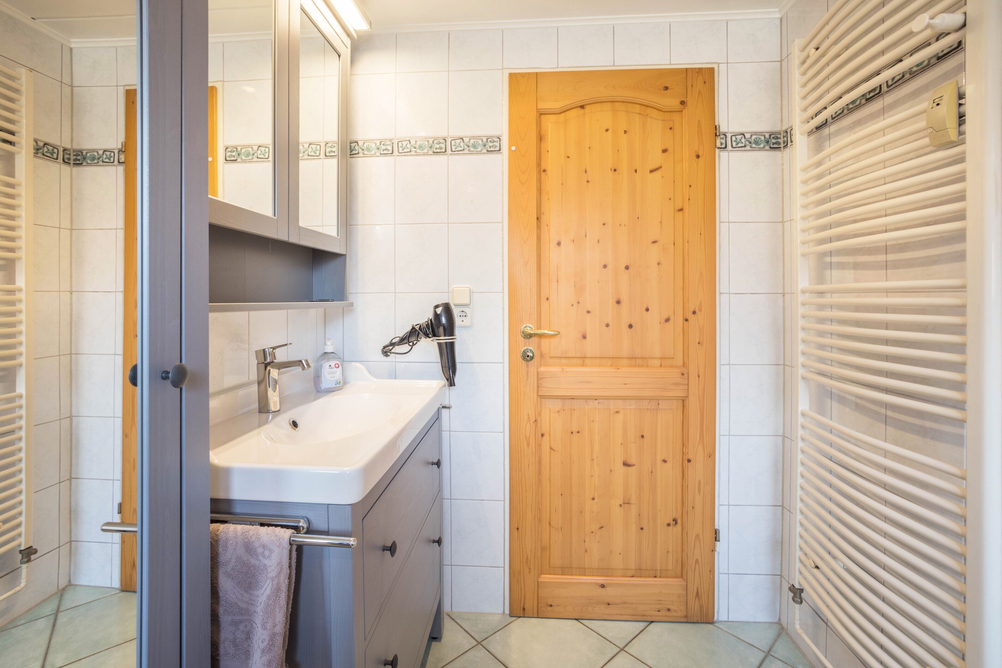 Ein Badezimmer mit Holztür, Waschbecken mit Spiegel und Handtuchhalter.