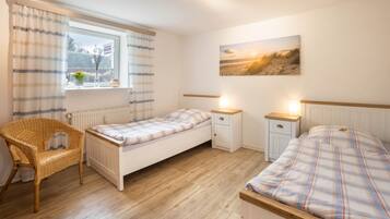 Une chambre avec un lit simple, une table de chevet, une chaise, une fenêtre avec des rideaux et un tableau accroché au mur.