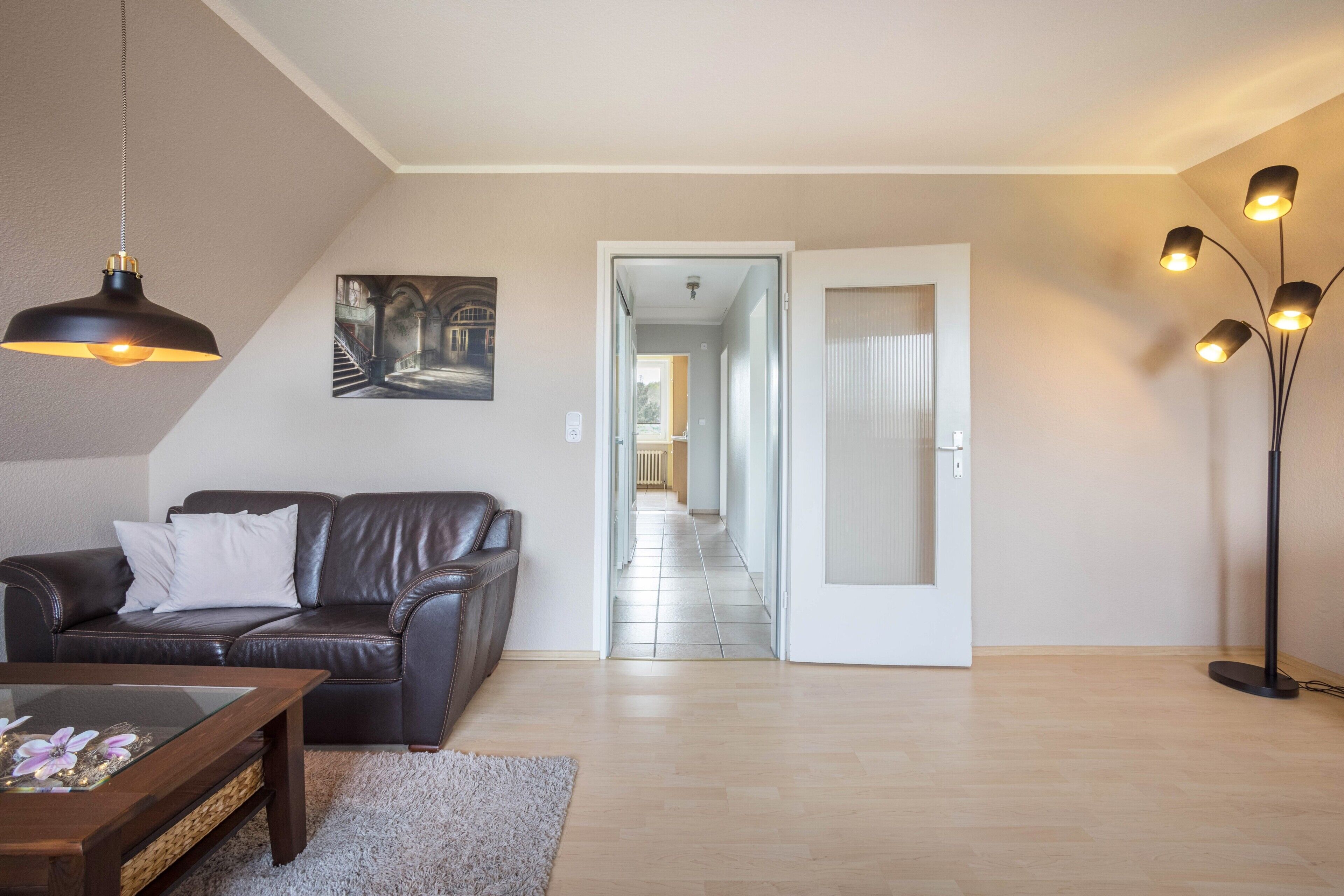 A living room with a sofa, a coffee table, a painting, and a hallway leading to another room.