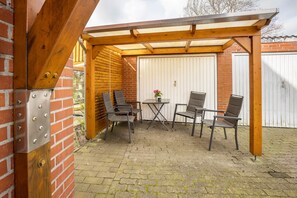 Un patio cubierto con pared de ladrillo, pérgola de madera y una mesa con cuatro sillas.