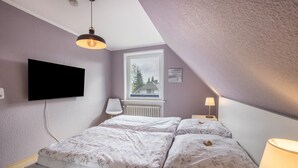 Quarto com cama, televisão na parede, janela com vista e luminária.