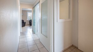 Corredor com porta de vidro deslizante, piso ladrilhado e vista para uma sala de estar com sofá e mesa de centro.