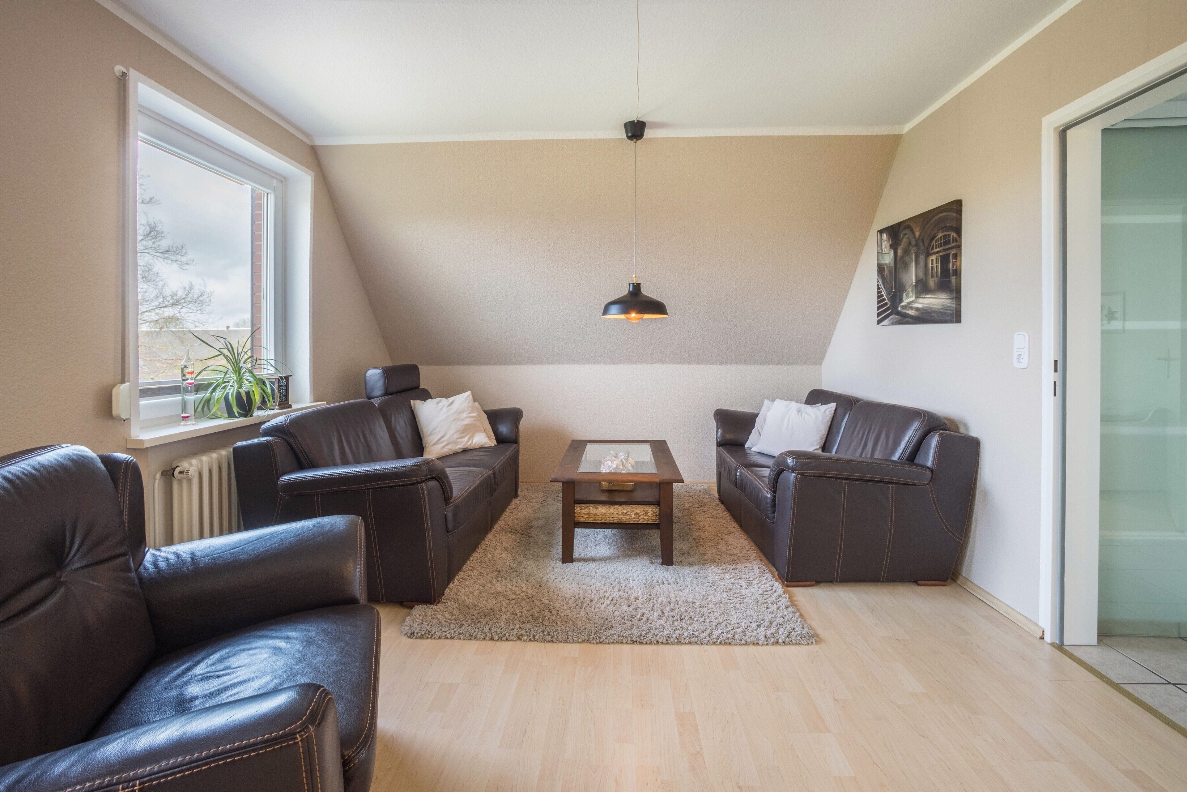 A living room with two leather sofas, a coffee table, a hanging pendant light, a window with a view, and a painting on the wall.