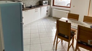 A compact kitchen with white cabinets, a blue refrigerator, a dining table with chairs, and a window with a view of the street. - Apartment 'Am Sonnenberg' with Private Terrace and Wi-Fi (Reichelsheim (Odenwald))