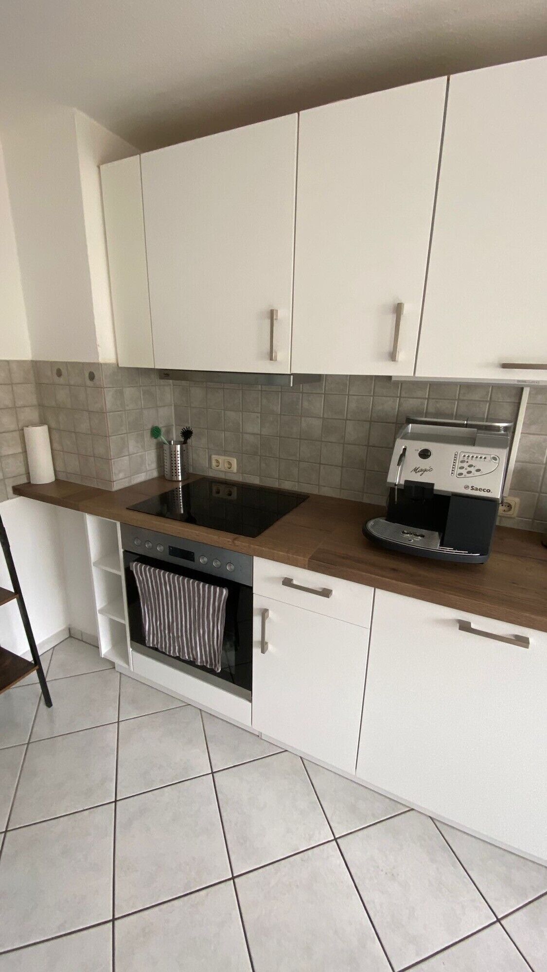 A kitchen with white cabinets, a built-in oven, a stovetop, and a coffee maker.