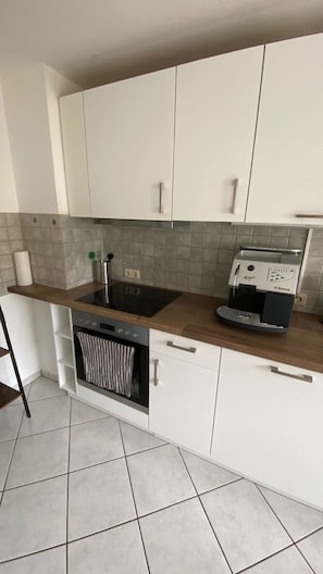 Una cocina con armarios blancos, horno empotrado, placa de cocina y cafetera.