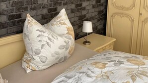 A bedroom with a brick-patterned wall, a bed with floral bedding, a bedside lamp, and a wardrobe. - Apartment 'Am Sonnenberg' with Private Terrace and Wi-Fi (Reichelsheim (Odenwald))