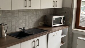 A kitchen with white cabinets, a black countertop, a microwave, and a window with a view. - Apartment 'Am Sonnenberg' with Private Terrace and Wi-Fi (Reichelsheim (Odenwald))
