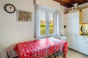 A kitchen with a dining area, a clock, and a window with a view of greenery.