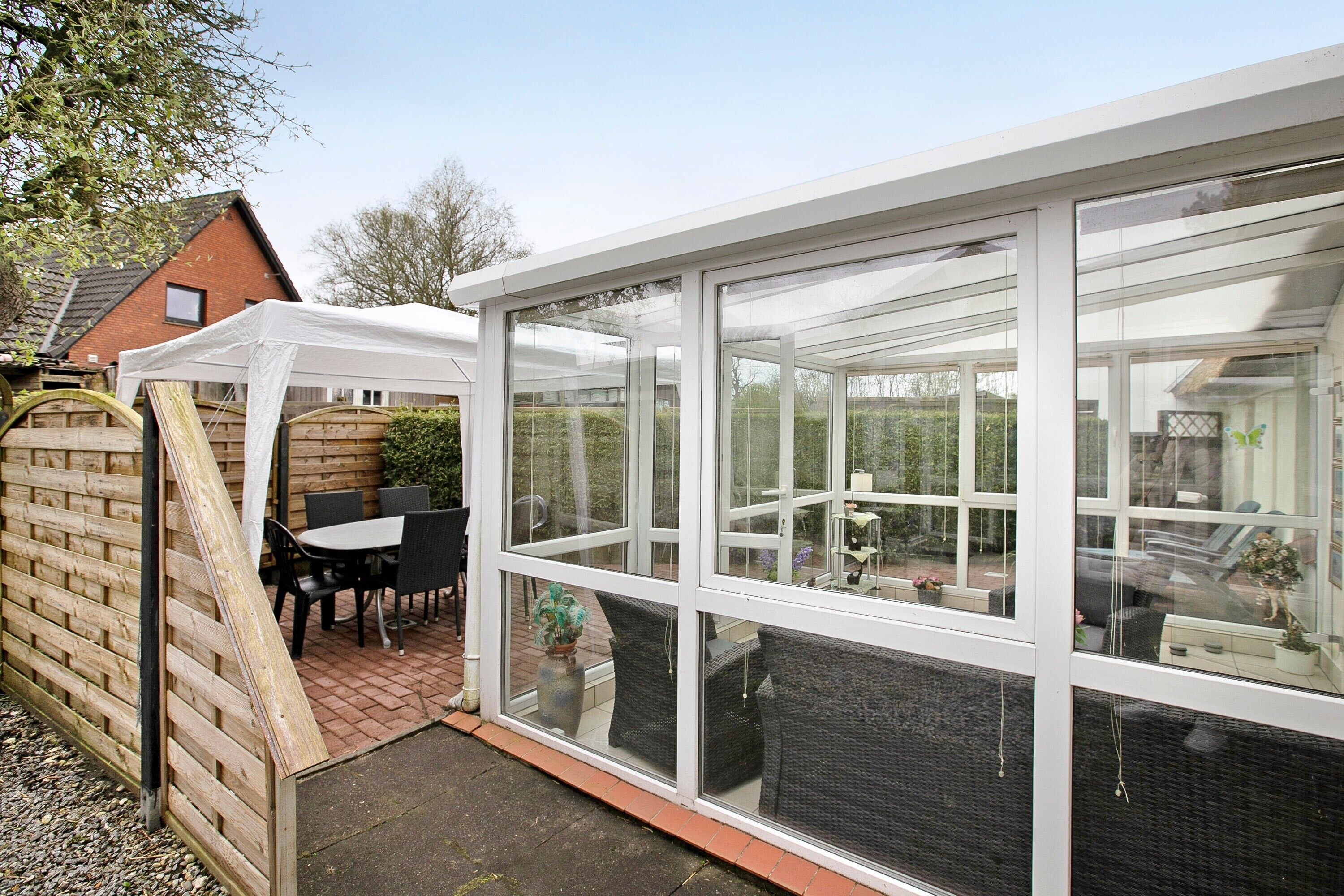 Ein Wintergarten mit Glasdach, Ziegelwand und einer Terrasse mit Gartenmöbeln.