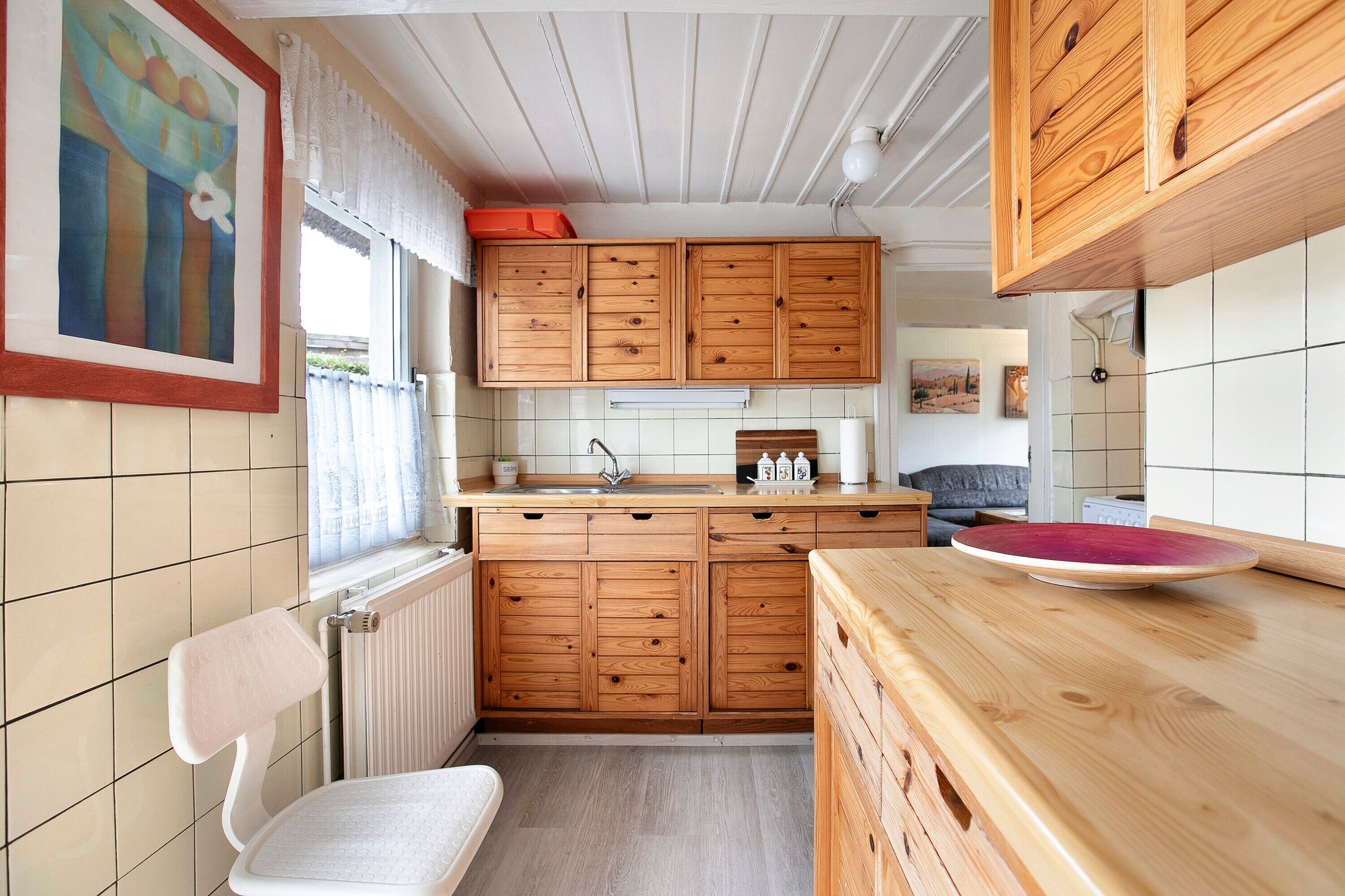 A kitchen with wooden cabinets, a white chair, and a window with curtains.