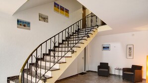 Uma escada com guarda-corrimão preto, uma porta branca e duas cadeiras de vime em um quarto com piso de azulejos.