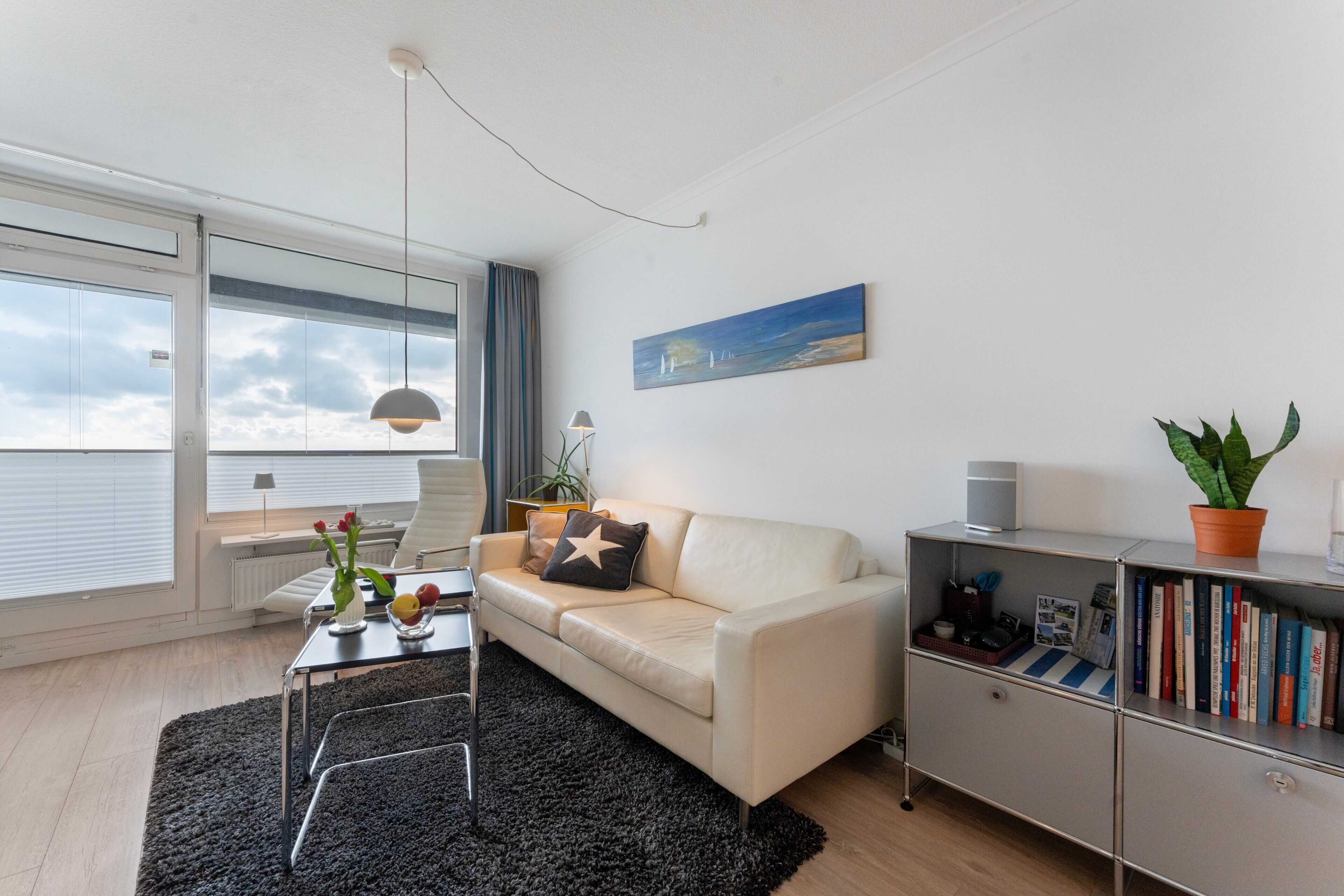 Ein modernes Wohnzimmer mit Sofa, Couchtisch, Bücherregal und einem Fenster mit Vorhängen.