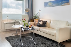 A modern living room with a white sofa, a black coffee table, a white chair, and a large window with a view of the sea. - Apartment 'Ostseeresidenz Damp - Ferienwohnung' with Sea View, Balcony and Wi-Fi (Damp)