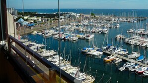 Un puerto deportivo con numerosas embarcaciones amarradas, cielo despejado y edificios al fondo.