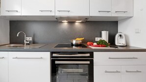 Una cocina moderna con armarios blancos, un lavamanos de acero inoxidable, un horno empotrado y una encimera con una olla y verduras.