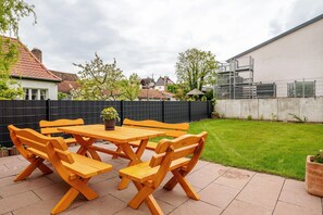 Eine Terrasse mit Holztisch und -stühlen, einem Blumentopf und einem gepflegten Rasen.