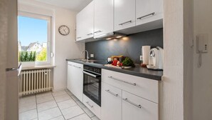 Una cocina moderna con armarios blancos, horno empotrado, ventana con vistas y un reloj en la pared.