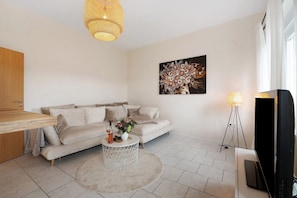 Un salon moderne avec un canapé, une table basse ornée de fleurs, une lampe et un téléviseur.