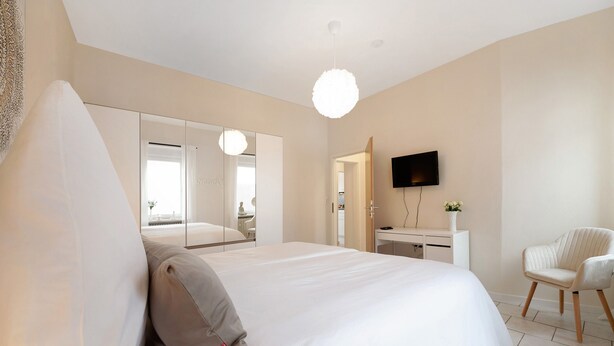 Un dormitorio moderno con una cama grande, televisión, una silla y un armario.