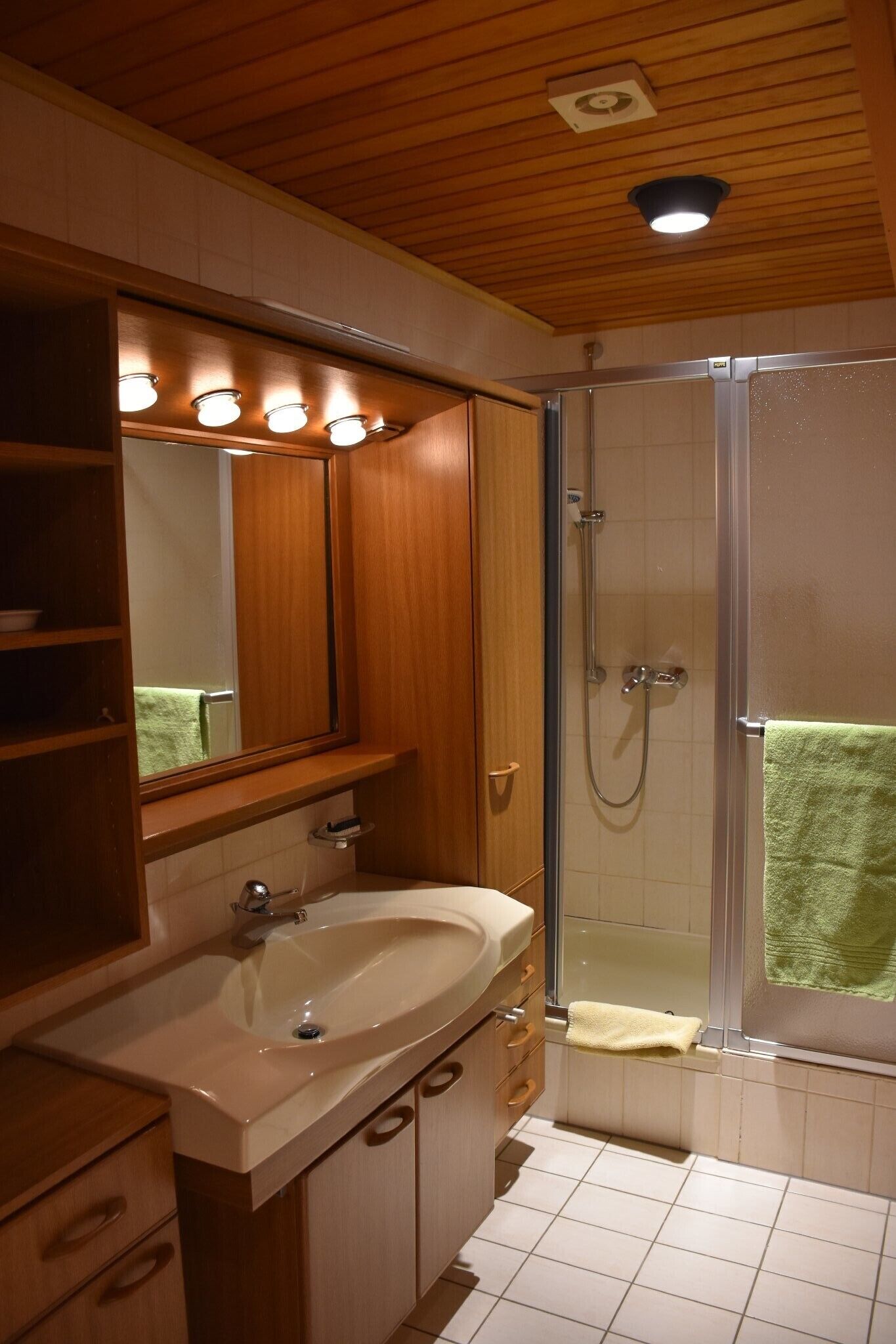 A bathroom with a wooden vanity, a sink, a mirror, a shower enclosure, and a towel rack.