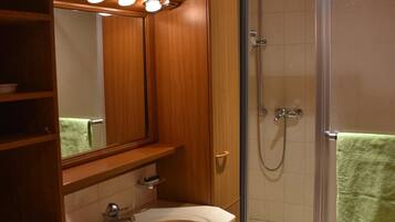 A bathroom with a wooden vanity, a sink, a mirror, a shower enclosure, and a towel rack.