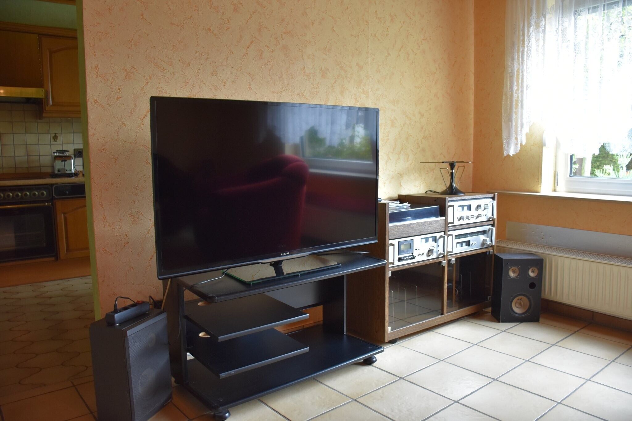 Ein Wohnzimmer mit Flachbildfernseher, einem roten Sessel, einem Couchtisch, einer Anrichte mit Audioanlage und einem Fenster mit Vorhängen.