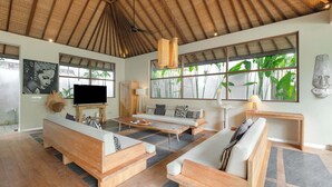 A spacious living room with a high ceiling, large windows, and a flat-screen TV. - Villa Nikaia by Villa Finder (Seminyak)