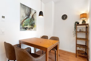 A dining area with a wooden table and leather chairs, a hanging pendant light, a wall clock, and a shelf with decorative items.