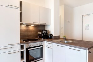 A modern kitchen with white cabinets, a built-in oven, a stove, and a coffee maker.