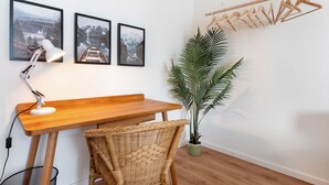 A wooden desk with a lamp, a wicker chair, a potted plant, and three framed pictures on the wall.