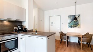 A compact kitchen with a built-in oven, a coffee machine, and a dining area with a table and chairs.