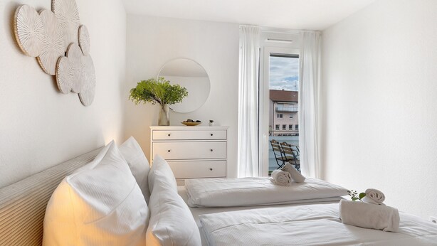 A hotel room with a bed, a dresser, a mirror, and a window with a view of buildings.