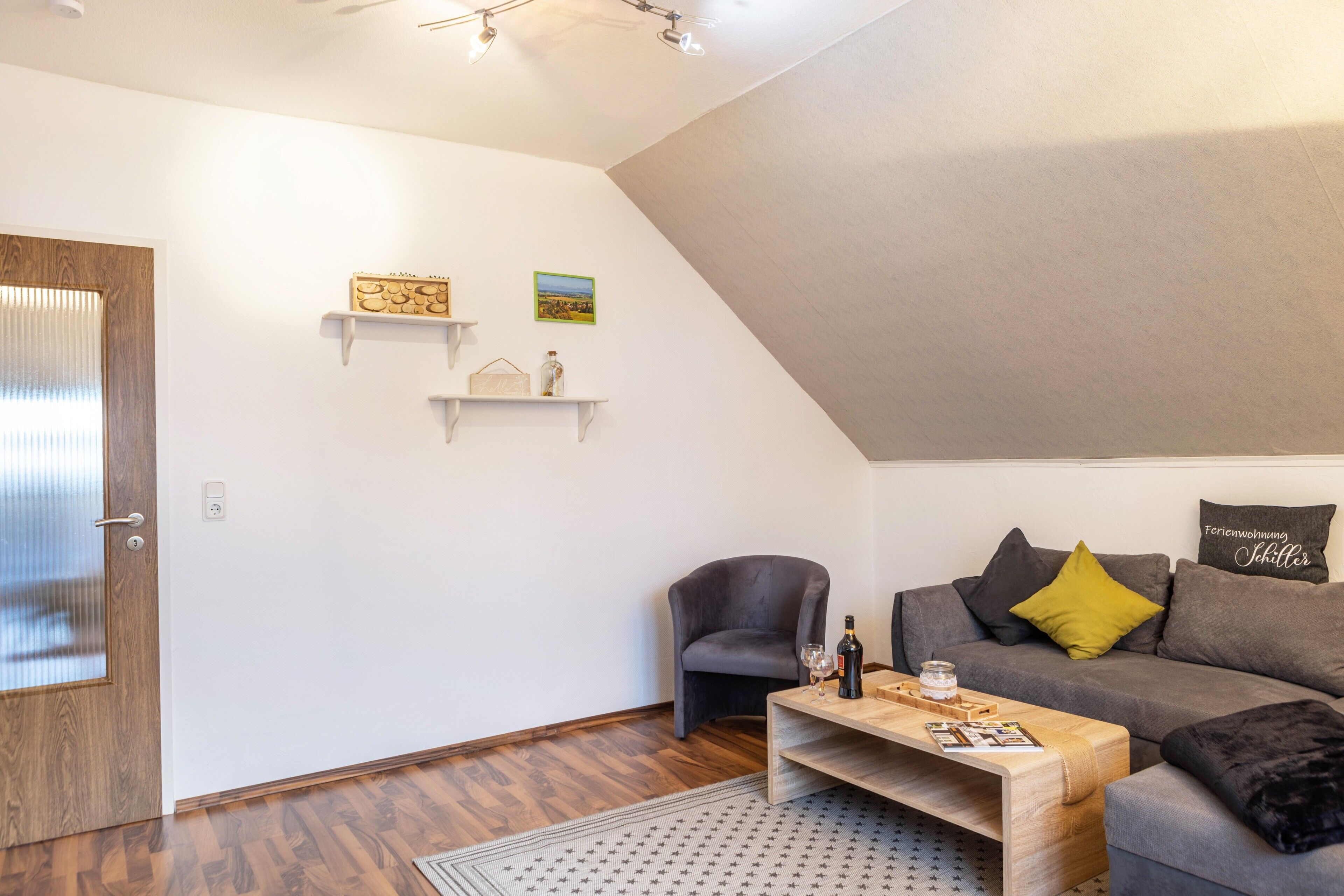 Una sala de estar moderna con piso de madera, un sofá gris con un cojín amarillo, una mesa de centro de madera y un sillón gris.