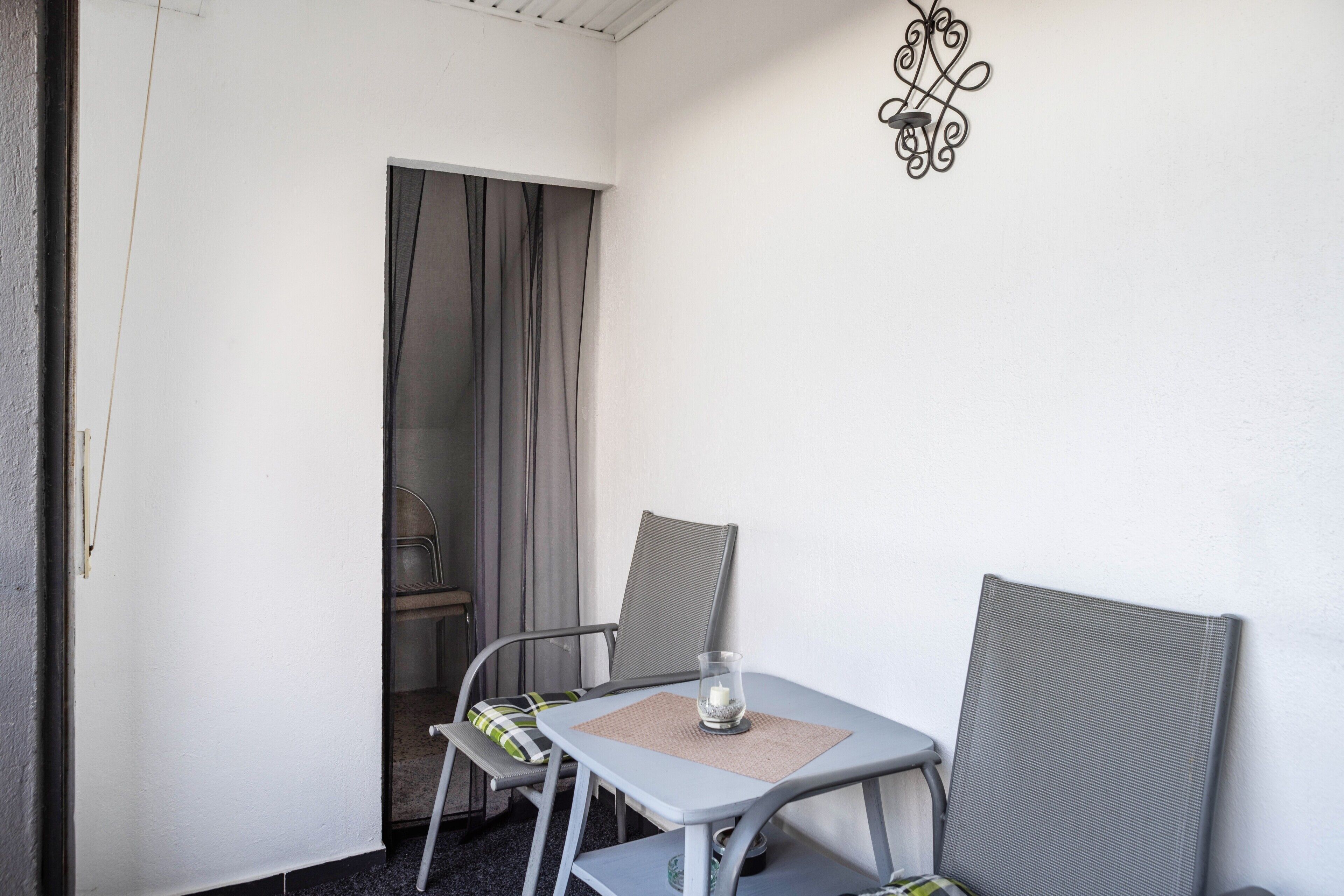 Een kleine kamer met een tafel, twee stoelen, een deur en een wandlamp.
