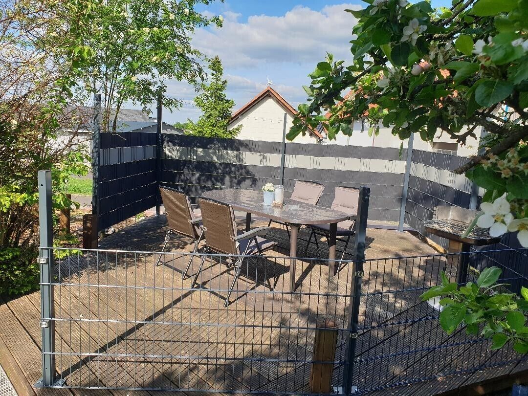 Un espace extérieur clos, aménagé avec une table et des chaises, une terrasse en bois et un bâtiment en arrière-plan.